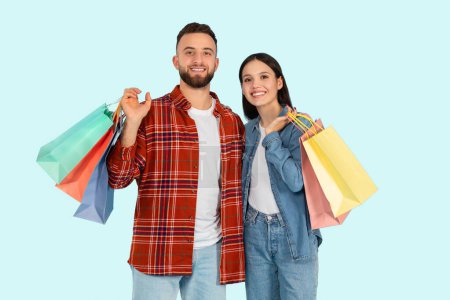 Smiling couple with multiple colorful shopping bags, presenting a consumer Zoomer lifestyle on blue background
