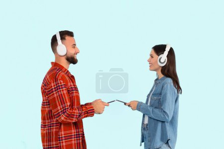 Téléchargez les photos : Homme et femme utilisant smartphones et écouteurs, écoutant de la musique, isolés sur un fond bleu clair - en image libre de droit