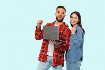 Foto de Una alegre pareja que sostiene un portátil muestra emoción, capturando el espíritu de la generación de Zoomer conectada, aislada en azul - Imagen libre de derechos