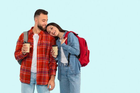 Foto de En esta imagen, una joven pareja cariñosa, parte de la generación z, sostiene tazas de café y disfruta de un momento juntos, aislados sobre un fondo azul - Imagen libre de derechos