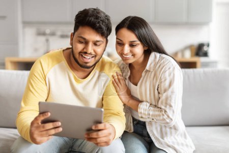 Foto de Una alegre pareja india joven está comprometida con una tableta, probablemente navegando o comprando en línea, exhibiendo unión e interacción digital - Imagen libre de derechos
