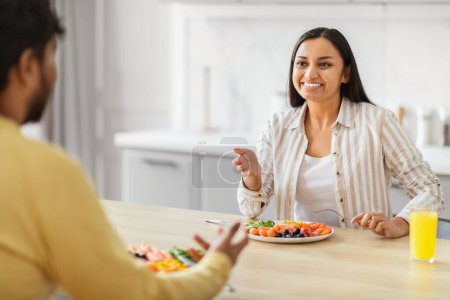 Photo for An Indian woman smiles engagingly in a kitchen setting, representing a modern millennial enjoying a loving chat with her spouse - Royalty Free Image