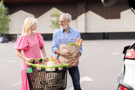 Das Bild zeigt ein älteres Ehepaar, das mit seinem Auto Lebensmittel verwaltet, und strahlt Routine und Zufriedenheit aus.