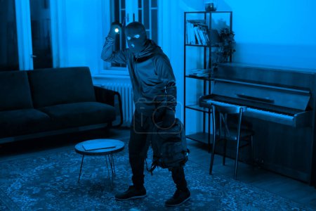 Die Silhouette eines Einbrechers, der eine Wohnung erkundet, wird während eines nächtlichen Einbruchs mit Taschenlampe in der Hand beim Diebstahl ertappt und symbolisiert Eindringen und Störung