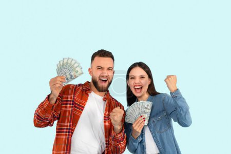 Foto de Un joven y una joven exhiben con entusiasmo su dinero, celebrando con una expresión alegre sobre un fondo azul - Imagen libre de derechos