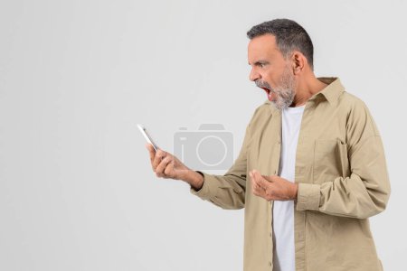 Téléchargez les photos : Un homme âgé est engagé avec son smartphone et criant, isolé sur fond blanc, affichant l'utilisation de la technologie parmi les anciens - en image libre de droit