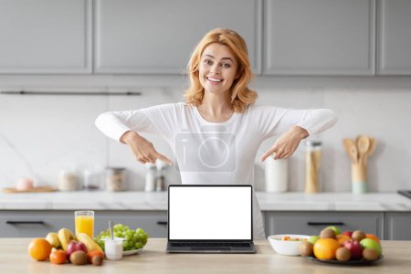 Photo for Enthusiastic pregnant European lady showcases something on a laptop screen, hinting at nutrition or pregnancy advice in the kitchen - Royalty Free Image