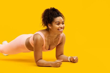 Photo for Engaged african american woman practicing a plank pose in fitness attire on an isolated yellow backdrop - Royalty Free Image