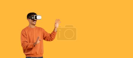 Téléchargez les photos : Le gars s'engage dans la réalité virtuelle, portant un casque VR et agitant avec désinvolture dans un contexte orange vif, copiant l'espace - en image libre de droit