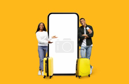 Photo for A smiling black couple standing next to a large smartphone mockup with a blank screen, perfect for travel application ads, isolated on a yellow background - Royalty Free Image