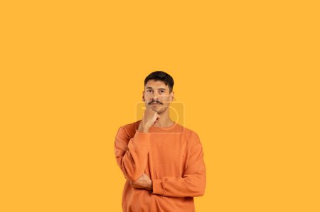 Photo for Pensive millennial with a moustache in a funny thoughtful pose, featured against a clean orange isolated background - Royalty Free Image
