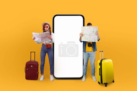 Foto de Un hombre y una mujer, presuntamente viajeros solitarios, parados con equipaje y un mapa, frente a un gran teléfono con una pantalla en blanco sobre un fondo amarillo brillante - Imagen libre de derechos
