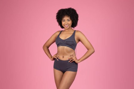 Photo for An African American sporty lady stands proudly isolated against a pink background, with her hands on her hips and a bright smile - Royalty Free Image