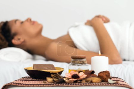 Eine Afroamerikanerin zeigt bei einer Wellness-Massage mit ätherischen Ölen und Kerzen Ruhe