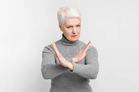 Une femme européenne âgée, âgée, faisant un signe X avec ses bras, indiquant qu'elle n'a pas ou s'arrête pour s3niorlife