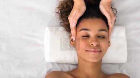 A relaxed African American lady enjoys the soothing benefits of a professional head massage in a spa environment