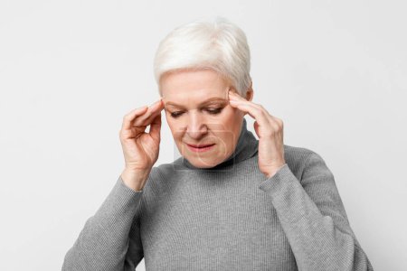Dieses Bild zeigt eine europäische Seniorin mit Kopfschmerzen, die auf ihre Schläfen drückt, und repräsentiert die häufigen gesundheitlichen Probleme von Senioren im s3niorlife