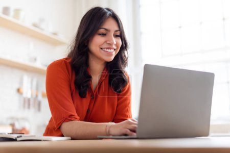 Téléchargez les photos : Une femme du Moyen-Orient semble engagée dans son travail sur un ordinateur portable à la maison, concept d'entrepreneuriat - en image libre de droit
