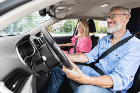 Téléchargez les photos : Couple marié retraité âgé dans une voiture pendant un trajet de jour, l'homme âgé se concentrant sur la route et la passagère regardant - en image libre de droit