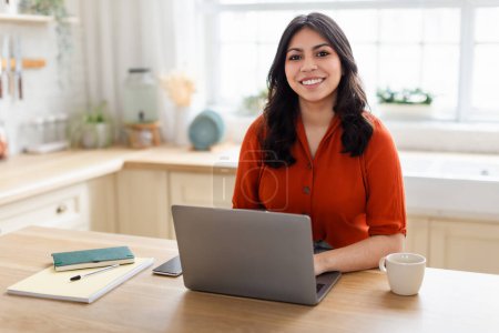 Eine Frau aus dem Nahen Osten strahlt Glück aus, während sie zu Hause an ihrem Laptop arbeitet, was den Lebensstil der Zoomer widerspiegelt
