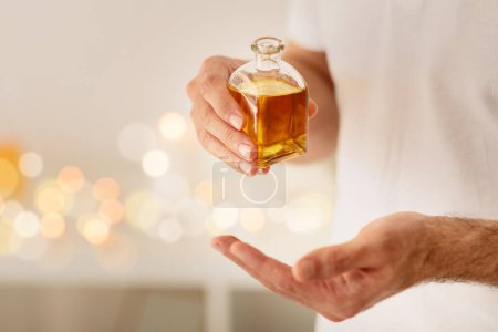 Une personne est capturée tenant une bouteille en verre d'huile de massage dorée, avec un fond bokeh suggérant un environnement spa luxueux