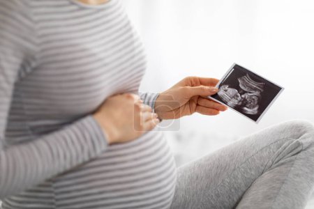 Téléchargez les photos : Une femme enceinte européenne à la maison, tenant une échographie, sentant la joie de sa maternité à venir, capturant le beau voyage de la grossesse - en image libre de droit