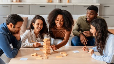 Téléchargez les photos : Un groupe de jeunes multiraciaux sont engagés dans une activité ludique, profitant d'un jeu de blocs empilables ensemble à la maison - en image libre de droit