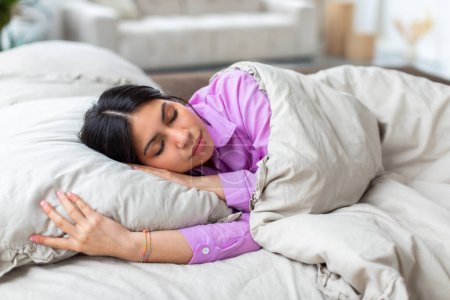 Eine arabische muslimische Frau zu Hause, die unter einer Bettdecke liegt und den Lebensstil des Nahen Ostens und den Komfort hervorhebt, in ihrem persönlichen Raum zu sein