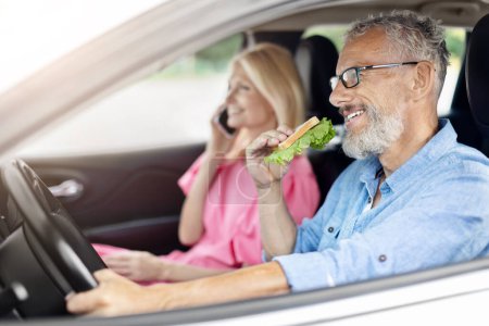 Foto de Una pareja de ancianos, jubilados y casados comparte un sándwich de ensalada fresca, disfrutando de un día tranquilo en la comodidad de su coche, promoviendo hábitos alimenticios saludables entre los ancianos - Imagen libre de derechos