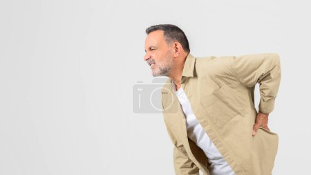 Photo for A senior man looks uncomfortable as he holds his back, showing the common physical struggles like back pain that old, retired individuals often face, isolated on white, copy space - Royalty Free Image