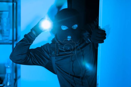 Téléchargez les photos : Une image représentant un voleur avec une lampe torche illuminant son visage la nuit, créant une atmosphère étrange de crime et de secret dans un appartement confines - en image libre de droit