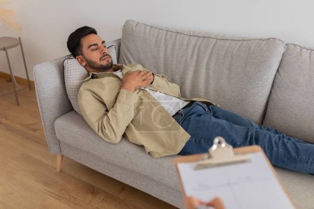 In einem zeitgenössischen Therapieumfeld liegt ein junger Mann auf einer Couch und diskutiert möglicherweise während einer Sitzung mit einem Therapeuten über seine Ehe
