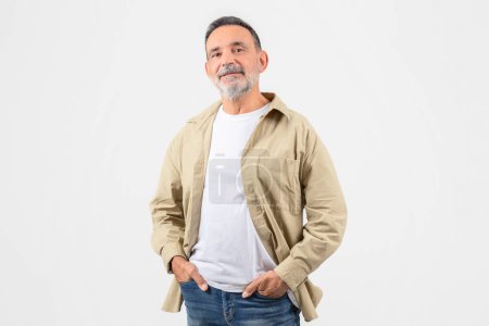 Photo for A cheerful older man with a grey beard smiles confidently, wearing a beige jacket and a white t-shirt, standing against a white background - Royalty Free Image