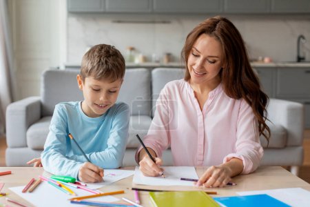 Photo for A warm European family scene portraying the affection and strong relationships between a mother and son as they share a love for drawing at home - Royalty Free Image
