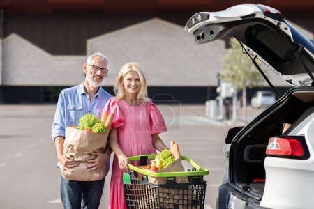 Couple marié âgé et retraité souriant à côté de leur voiture avec un panier rempli d'épicerie, représentant un mode de vie sain et actif