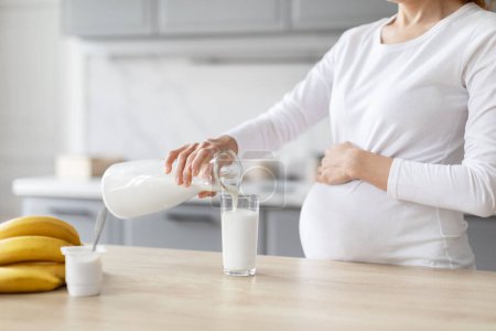 Photo for A european pregnant lady is pictured in the kitchen focusing on nutrition as she pours milk into a glass, surrounded by fresh fruit - Royalty Free Image