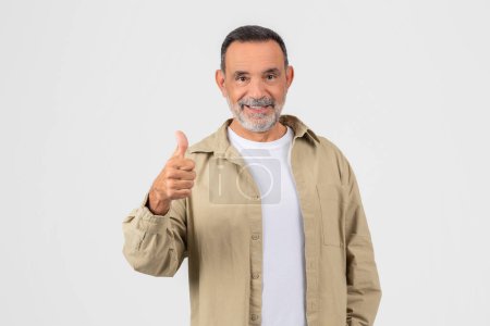 Confident elderly man showing thumbs up with a friendly smile, isolated on a white background, represents approval