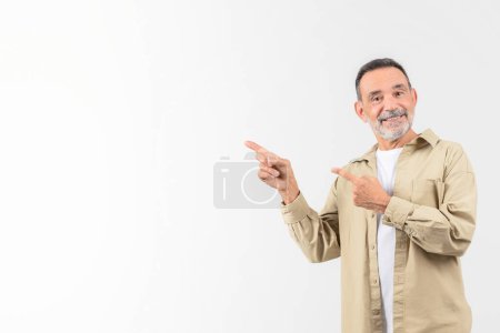 Foto de Un anciano con atuendo casual sobre un fondo blanco apunta hacia un lado, posiblemente indicando un producto o idea, con una sonrisa segura, espacio para copiar - Imagen libre de derechos
