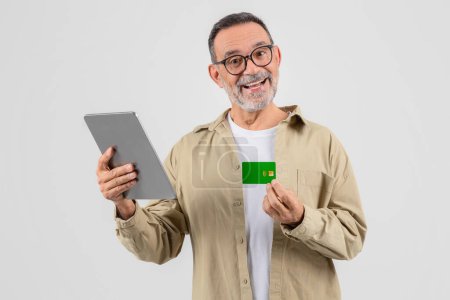 This image shows an elderly, sophisticated man holding a tablet in one hand and a credit card in the other, emphasizing old individuals interacting with modern finance