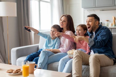 Foto de Mientras miran la televisión juntos, esta familia europea muestra amor y relaciones cercanas adivinando interactivamente lo que sucede a continuación, compartiendo un momento divertido en casa - Imagen libre de derechos