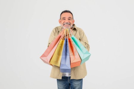 Ein älterer Mann strahlt vor Freude und hält bunte Einkaufstüten in der Hand, die auf weißem Hintergrund ein erfolgreiches Einzelhandelserlebnis suggerieren.
