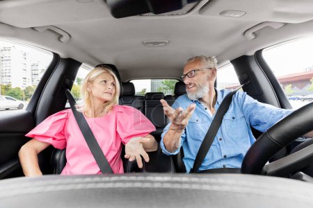 An older couple seems to be in a disagreement while the man is driving and the woman looks disapprovingly