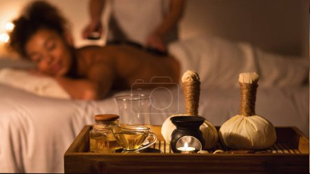 Foto de Una mujer afroamericana relajada recibe un masaje de espalda en un ambiente relajante spa con aceites esenciales y velas - Imagen libre de derechos