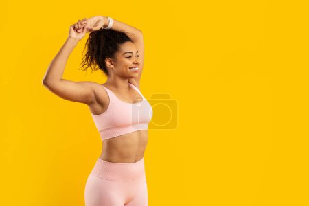 Foto de Una mujer afroamericana realiza un estiramiento mostrando flexibilidad y fuerza, aislado sobre un fondo amarillo para un tema de fitness - Imagen libre de derechos