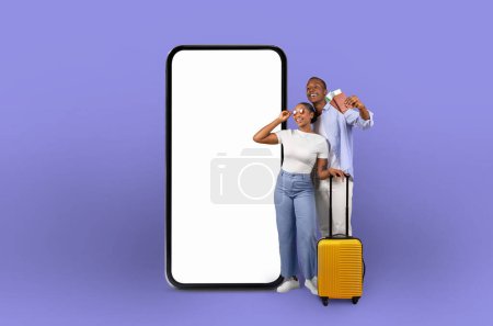 Photo for African american couple next to an oversized smartphone, representing the impact of technology and digital applications on travel planning and online offers - Royalty Free Image