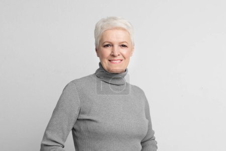 Photo for Charming short-haired elderly woman with a warm smile posing on grey background, ideal for s3niorlife content - Royalty Free Image