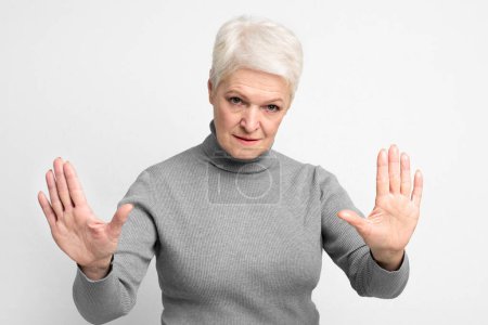 A senior, elderly european woman with arms raised in a stopping motion, emphasizing boundaries for s3niorlife