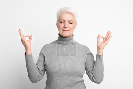 Photo for A serene senior, elderly European woman adopts a meditative pose, highlighting tranquility and s3niorlife balance - Royalty Free Image