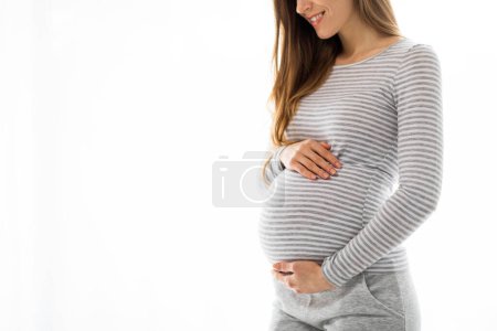 Une joyeuse femme enceinte en chemise rayée berçant doucement son ventre, représentant la beauté et l'anticipation de la maternité dans un cadre lumineux