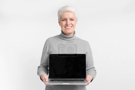 Photo for A senior European woman holding a laptop open with a blank screen, suitable for customization and linked with s3niorlifes tech-savvy approach - Royalty Free Image